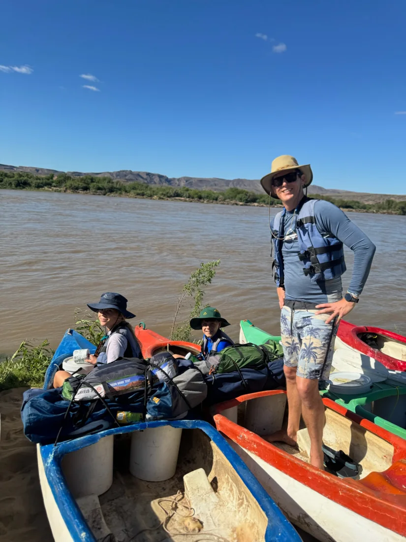 A parent and children in loaded canoes beside the Orange River